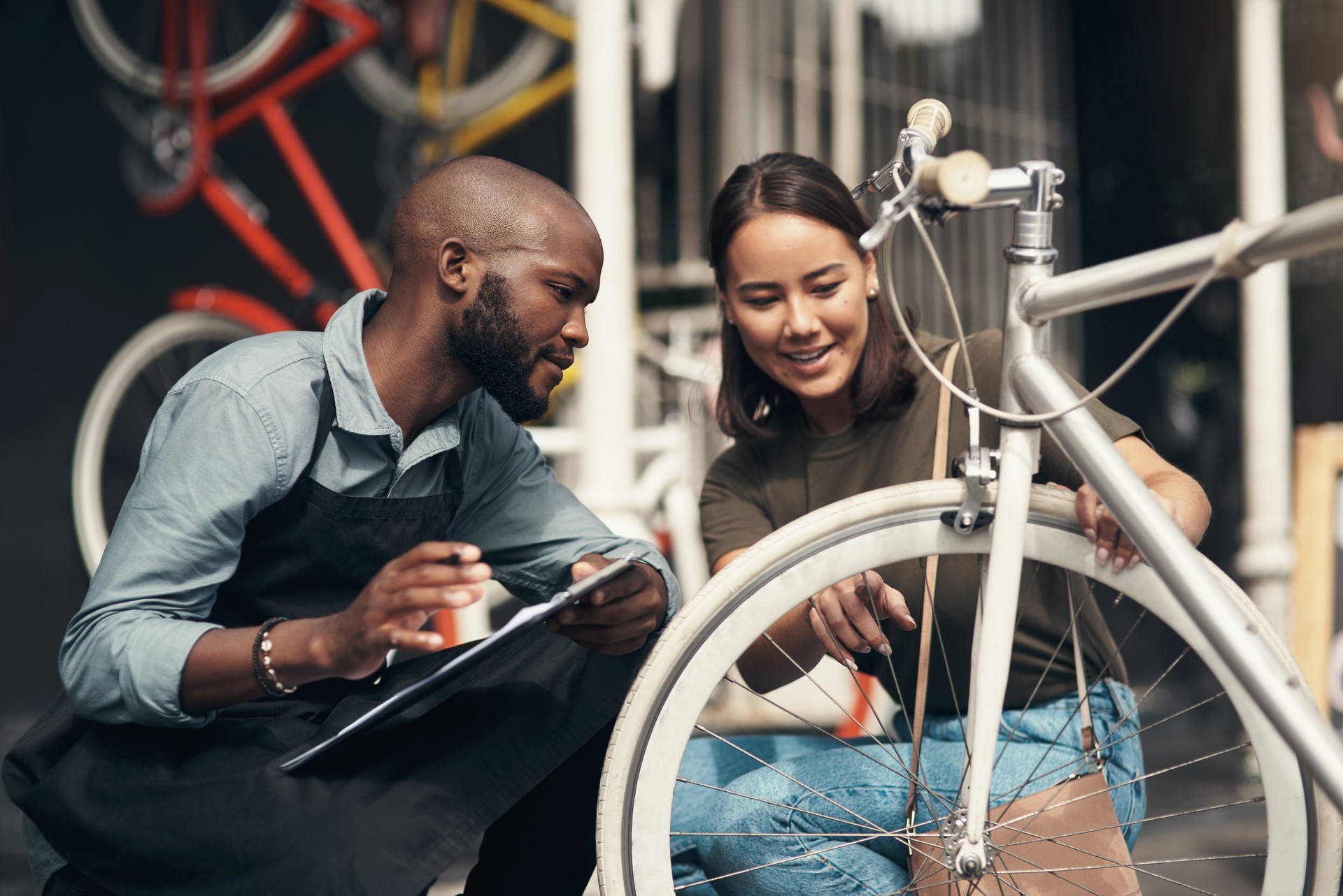 Shot of a handsome young man crouching outside his bicycle shop and assisting a customer